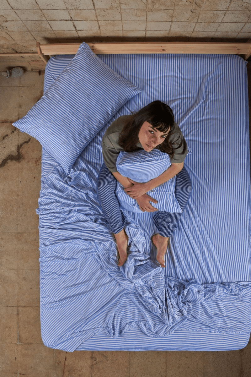Woman lying on bed wearing blue striped bamboo cotton sheet set from above view