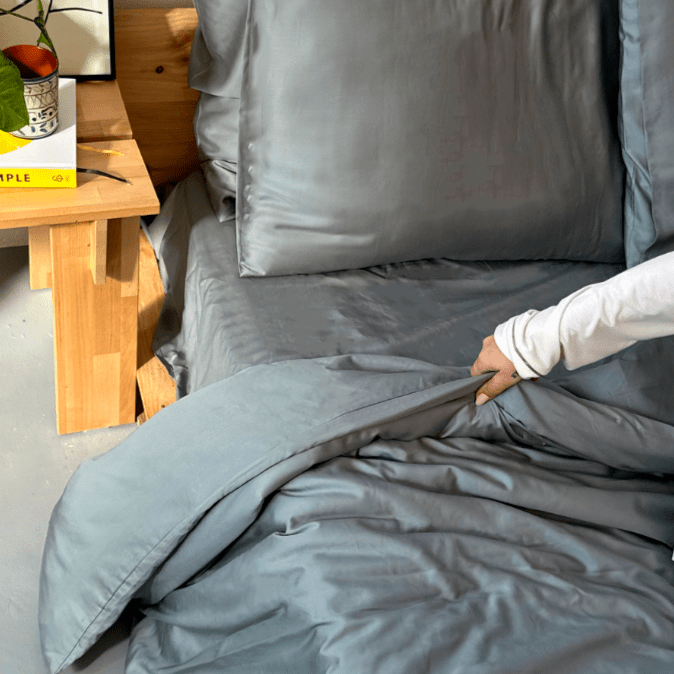 Woman touching grey bamboo bedding on bed with wooden table in background
