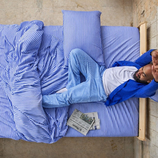 Man sleeping comfortably on blue and white striped bamboo sheets.