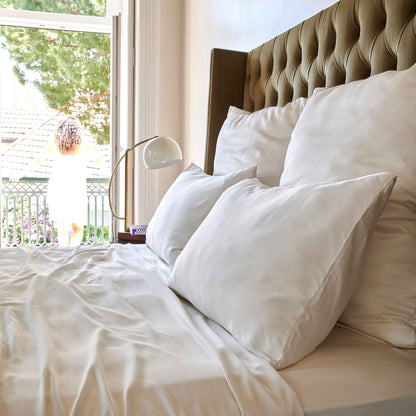 White bed sheet on bed with upholstered headboard by window overlooking garden