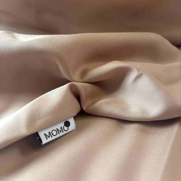 Folded beige bamboo fitted sheet with visible momo-cotton label, showing soft texture and fabric drape