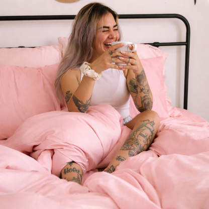 Woman lying comfortably on pink bamboo sheets, emphasizing the silky feel and gentle drape.